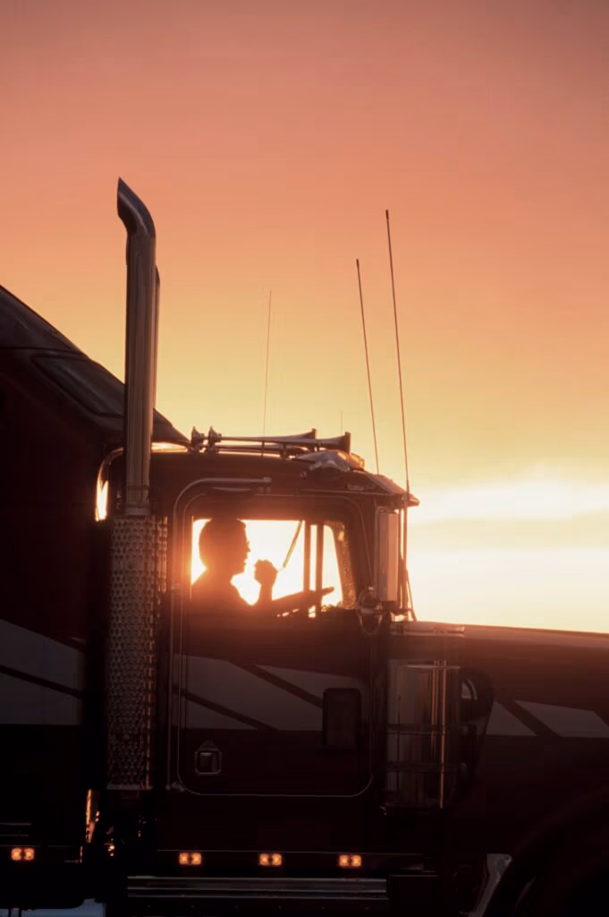 A silhouette of a truck driver on his CB radio in the cab of his Class 8 truck.