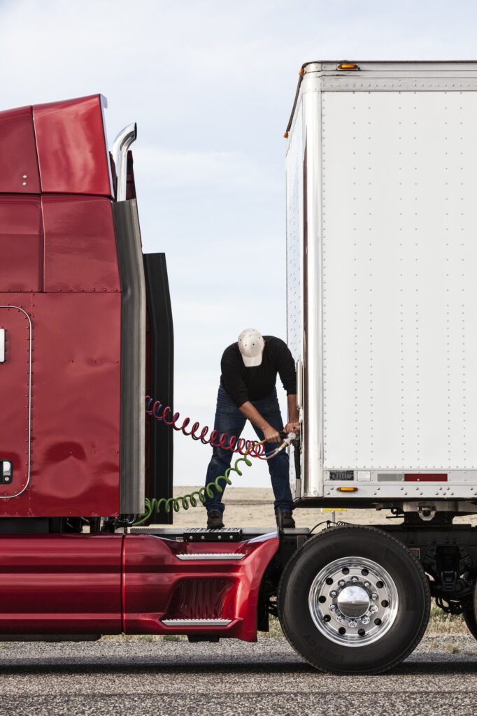 View of a driver connectiing the power cables to trailer of a commercial truck.
