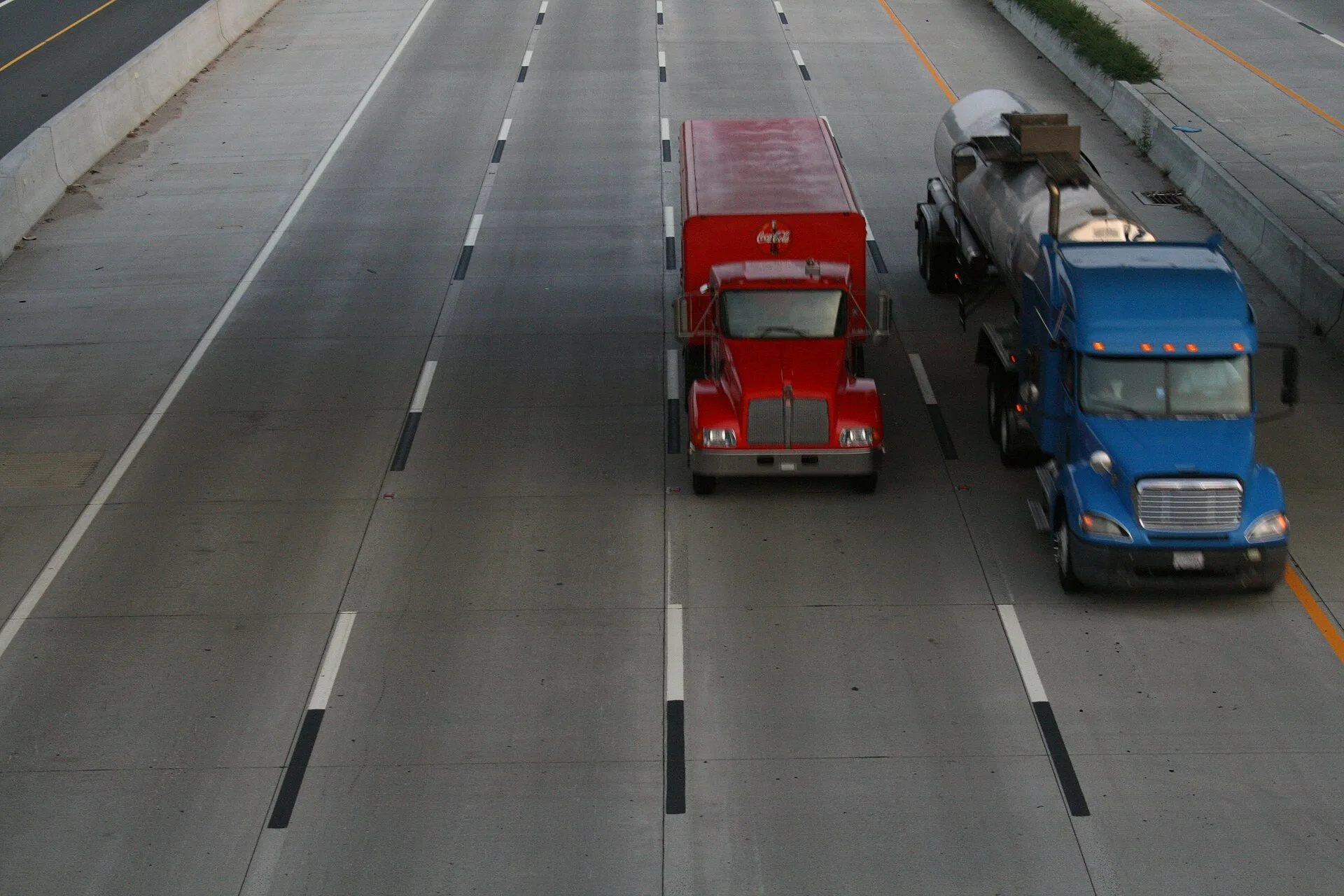 Two tractor-trailers driving side by side on a multi-lane interstate highway