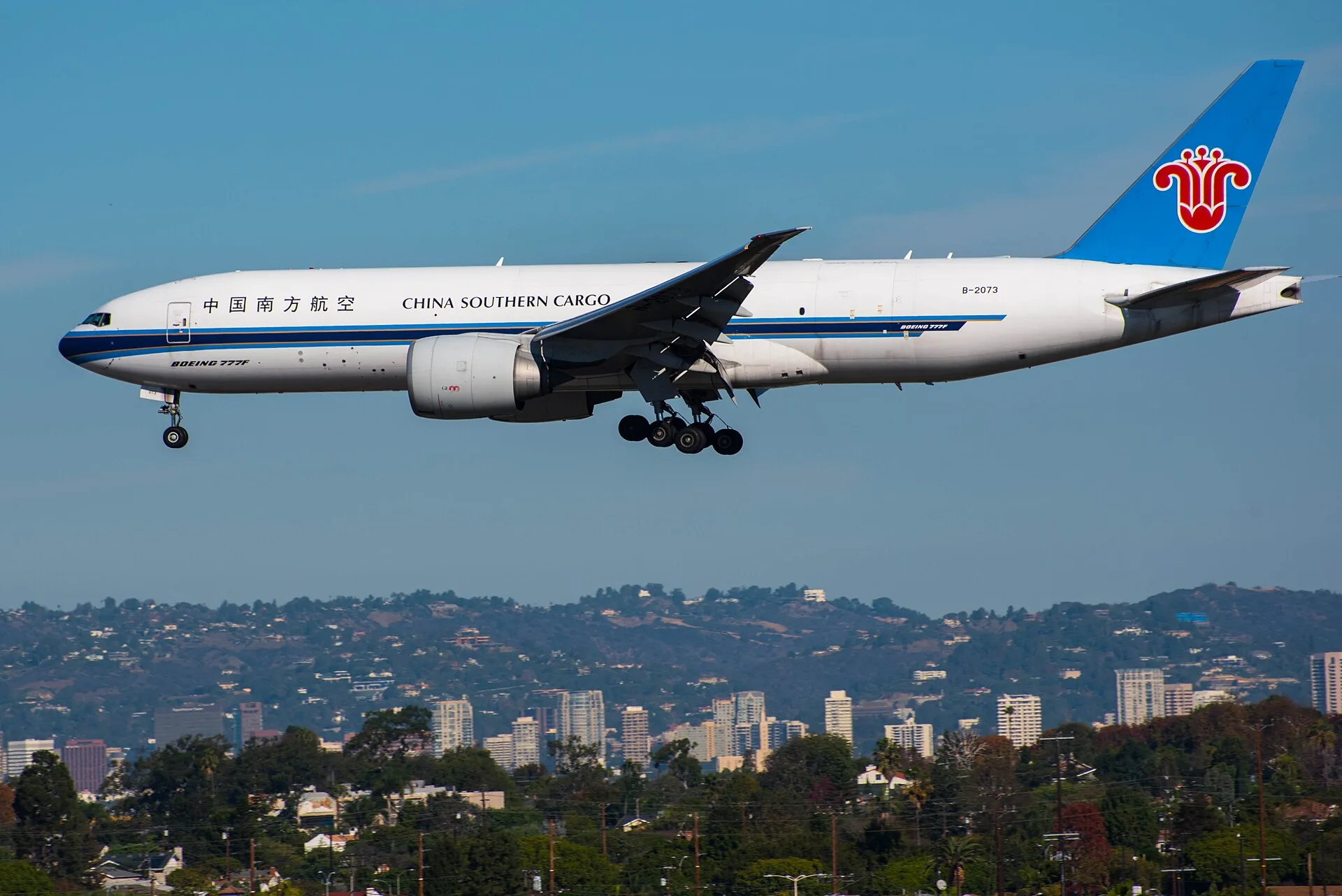 Boeing 777 freighter descending toward Los Angeles International Airport with the city hills behind it