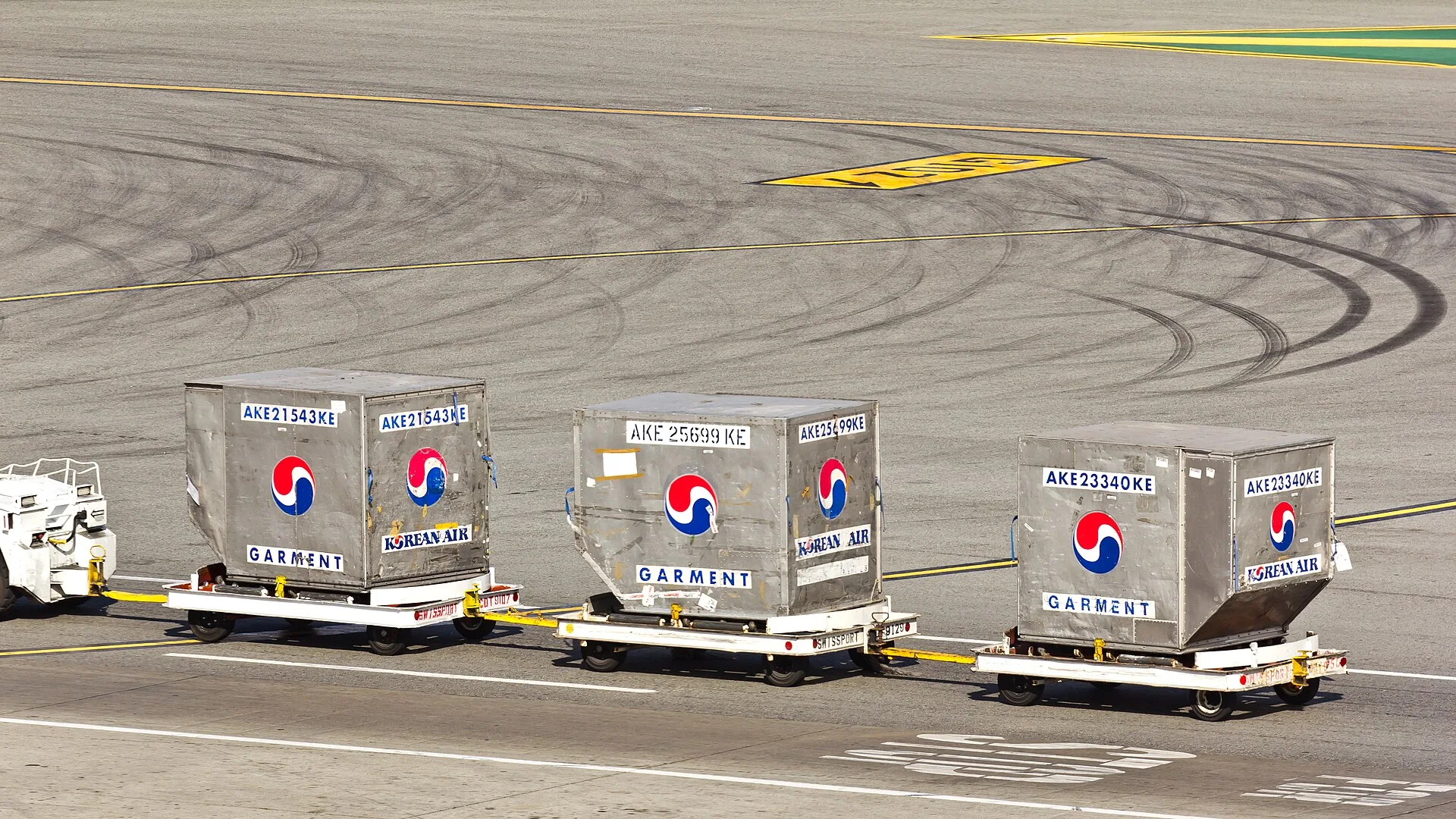 Three air cargo unit load devices (ULD containers) on dollies being towed across an airport apron
