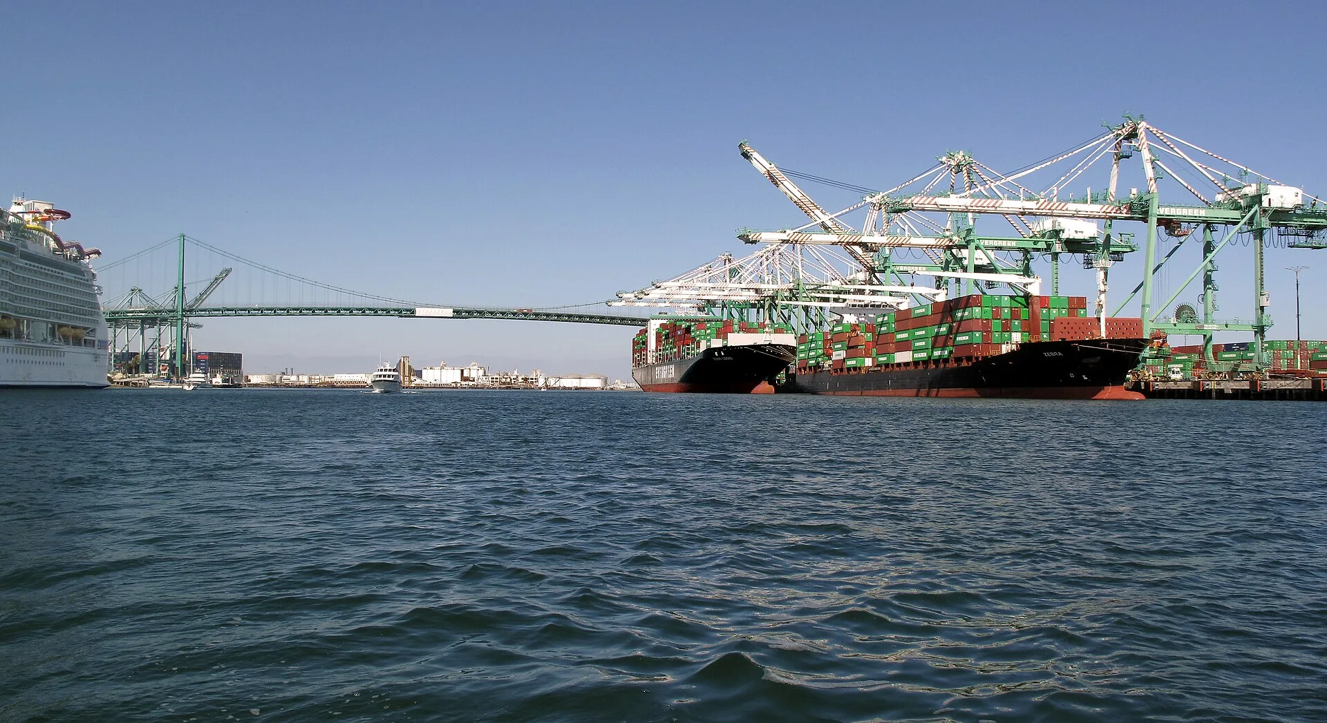 Container ships being worked by cranes at the Port of Los Angeles with the Vincent Thomas Bridge behind